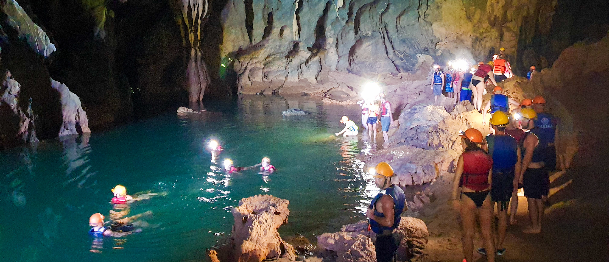 Adventurers with headlamps explore Phong Nha's mysterious Dark Cave, swimming in its turquoise underground lake.