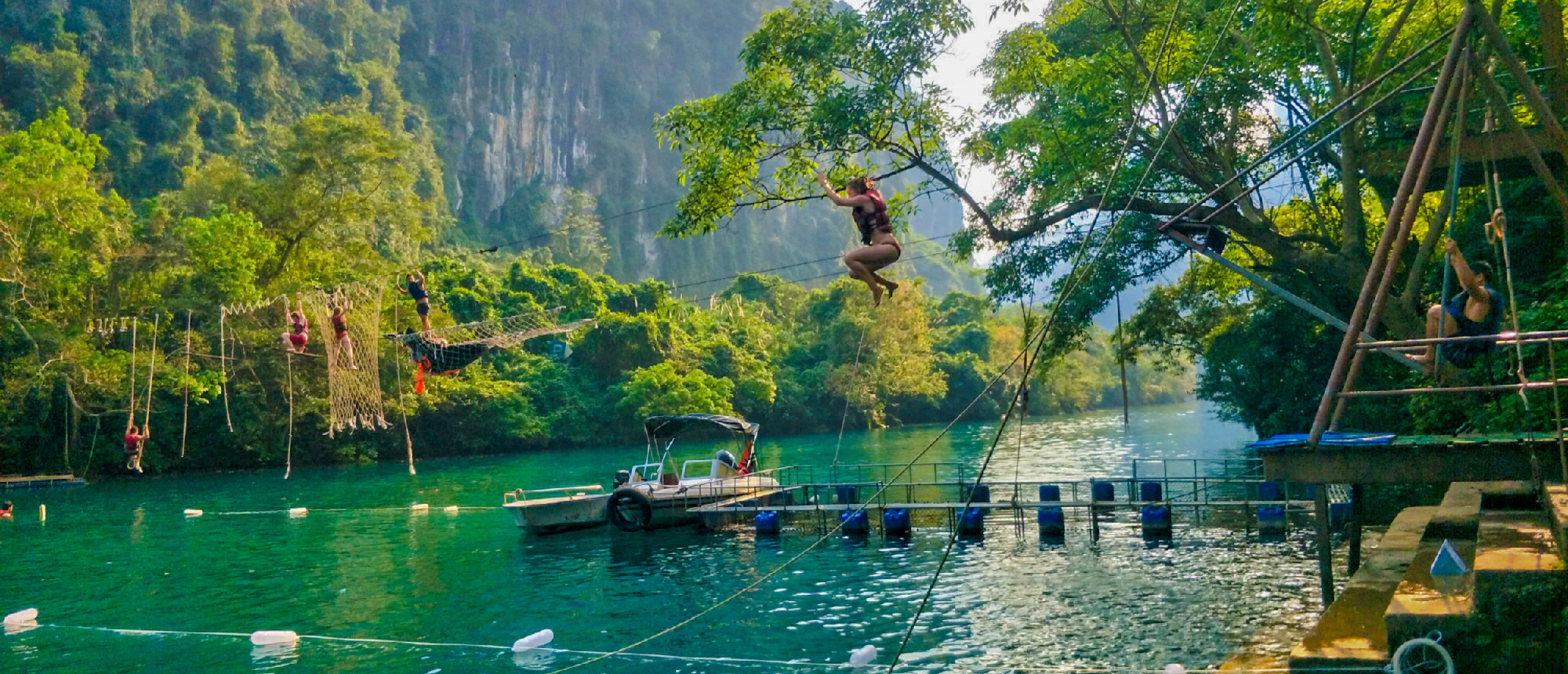A person jumps from a rope swing into the clear green water of Phong Nha, surrounded by jungle.