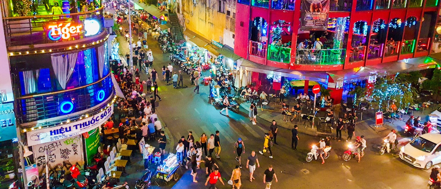 A vibrant Ho Chi Minh City street at night, bustling with people, motorbikes, and colorful neon lights.