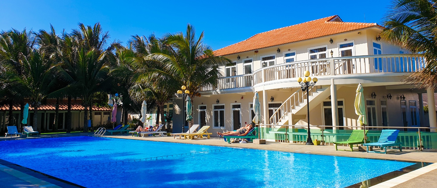 Guests relax by the sparkling blue pool at a tropical resort in Mui Ne, Vietnam.
