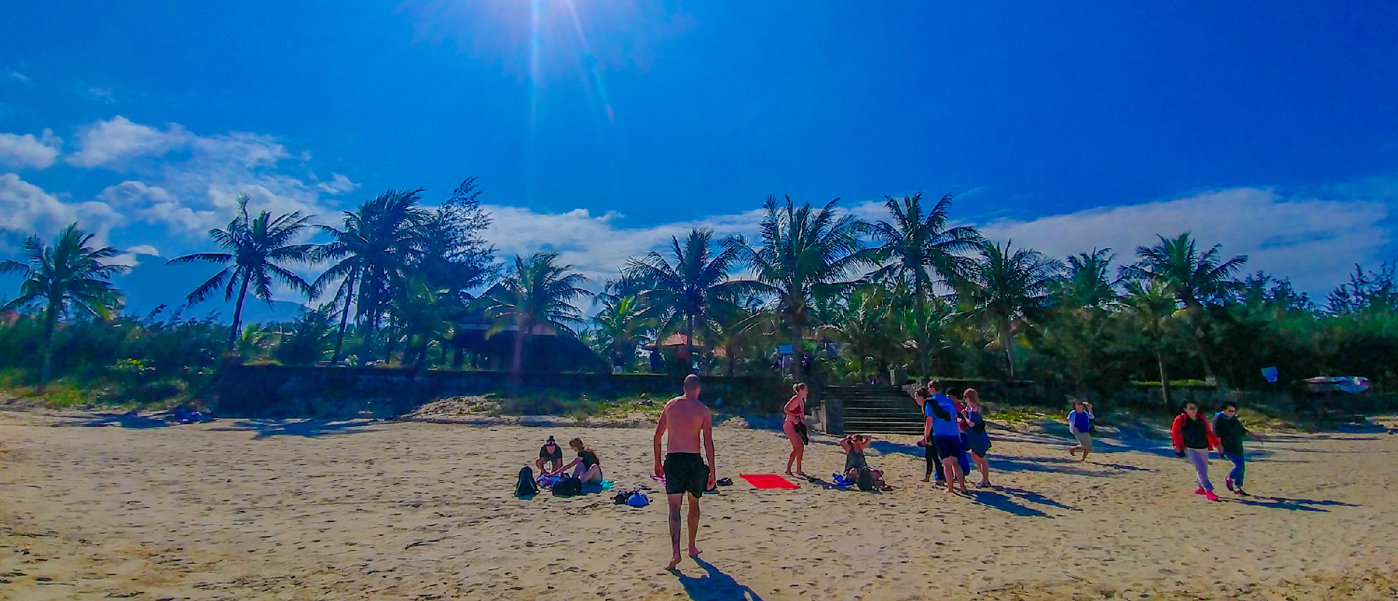 Tourists enjoying a bright day on the sandy beach of Nha Trang, surrounded by palm trees.