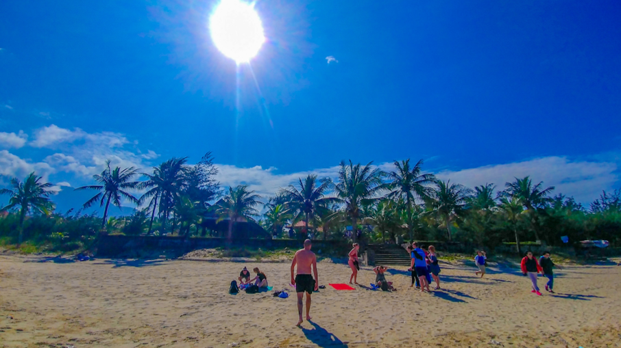 A group of people enjoying the bright sun and sandy beach with palm trees in Vietnam.