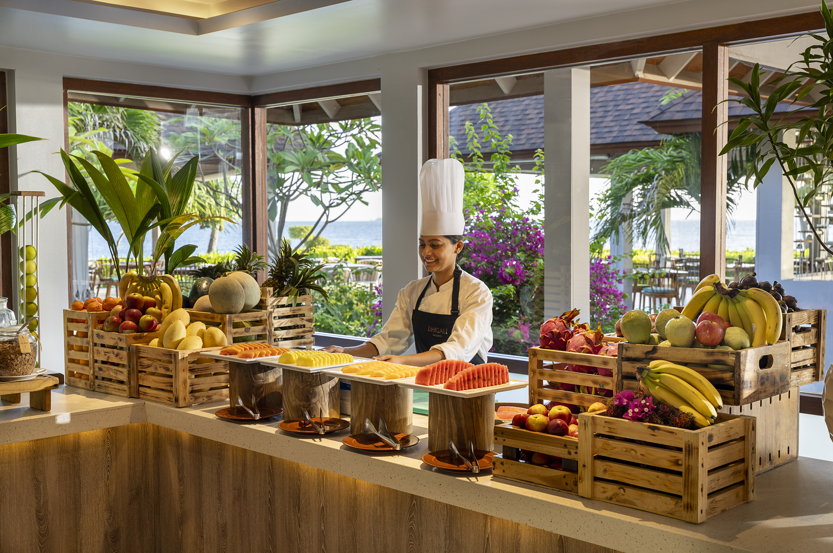 Smiling chef at an abundant fresh fruit buffet in a bright Maldives resort restaurant.