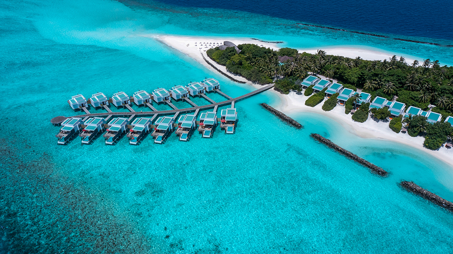 Luxurious overwater villas extend into turquoise water next to a white sand beach in the Maldives.