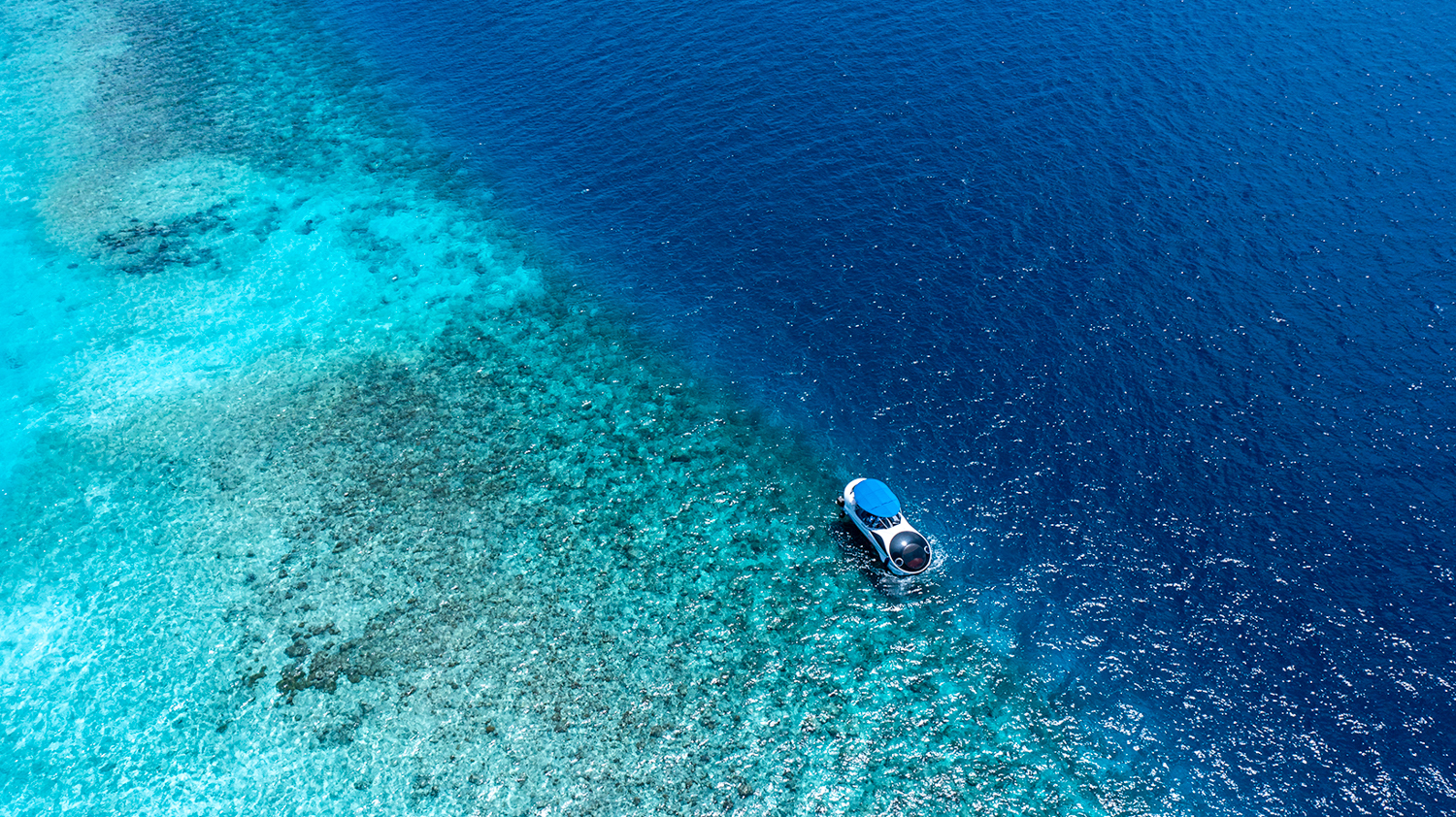 Aerial view of a semi-submersible boat exploring the clear turquoise waters of the Maldives.