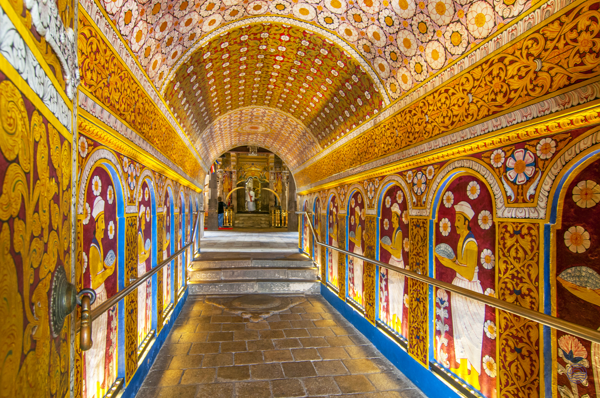 Vibrant golden and red murals adorn an ancient arched passage leading to a shrine in Sri Lanka.