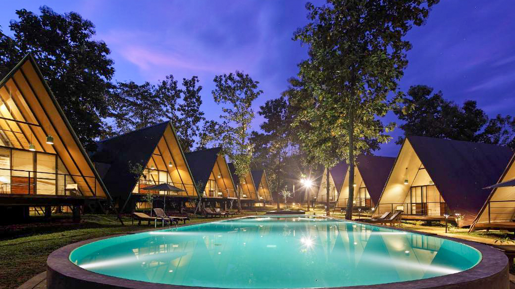 Serene resort with illuminated A-frame cabins and a circular swimming pool under a twilight sky.