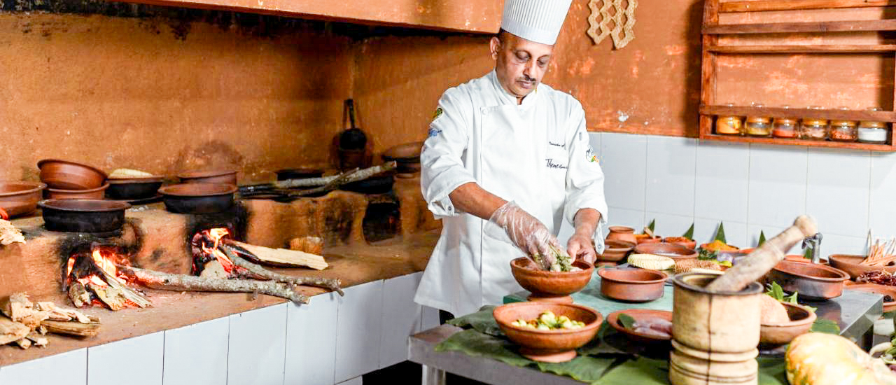 A chef in Kandy prepares fresh ingredients in a traditional kitchen with wood-fired stoves and clay pots.