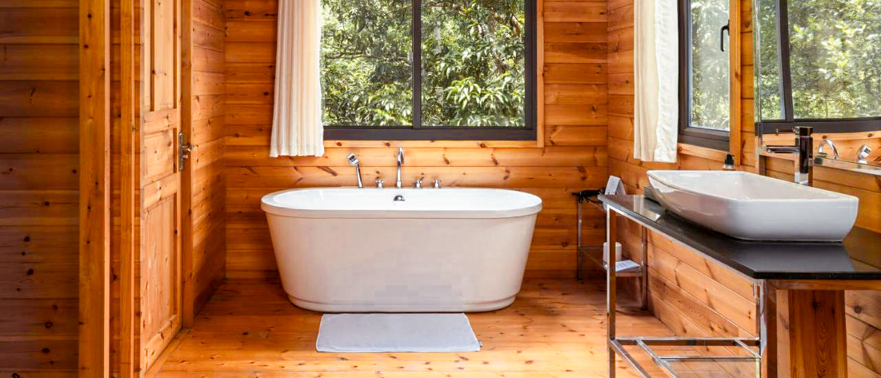 Peaceful wooden bathroom featuring a white bathtub and large window overlooking lush trees in Kandy.