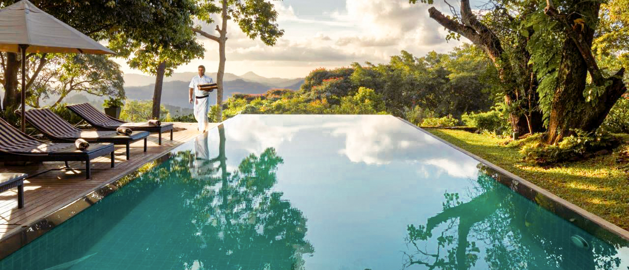 A staff member walks by an infinity pool overlooking lush green mountains in Kandy, Sri Lanka.
