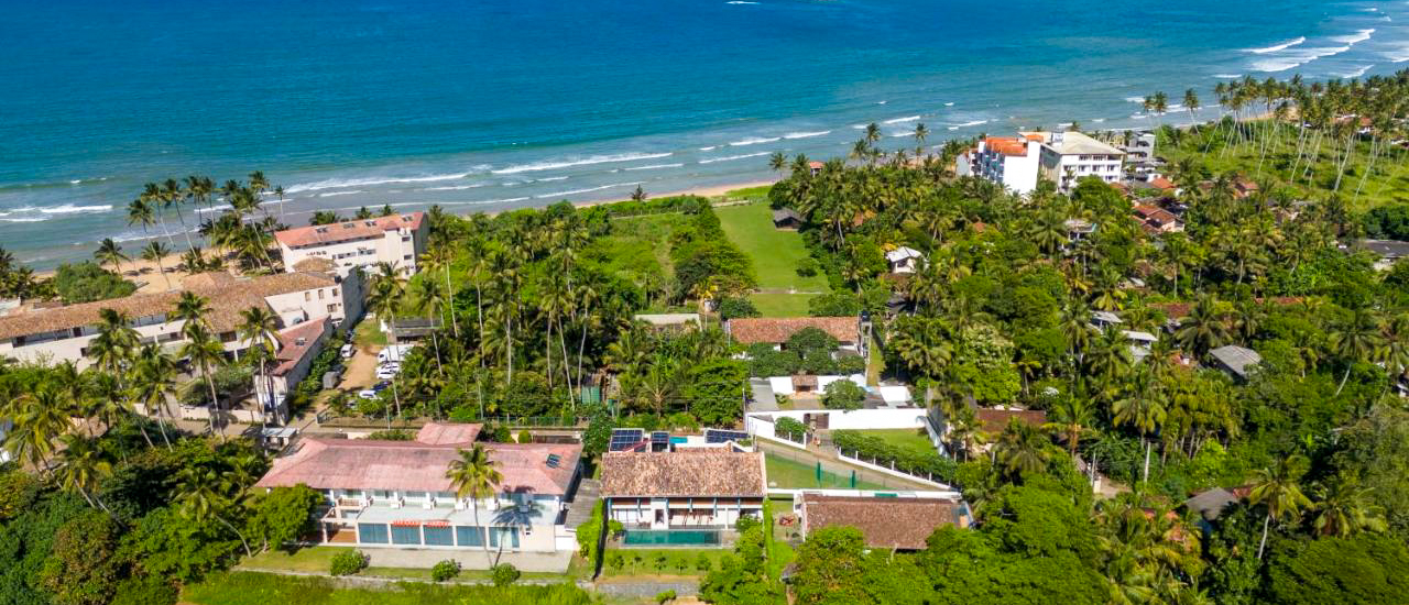 Aerial view of tropical villas and palm trees lining the beautiful blue ocean in Weligama.