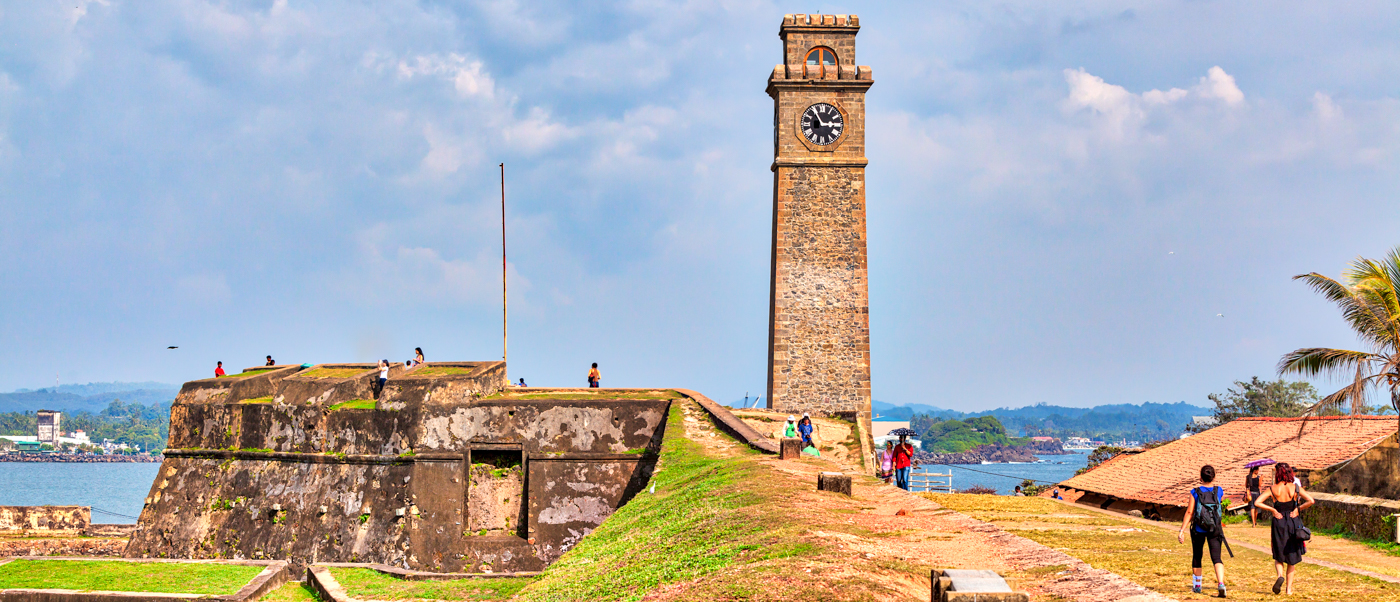 Tourists explore the historic Galle Fort with its iconic clock tower overlooking the sea.