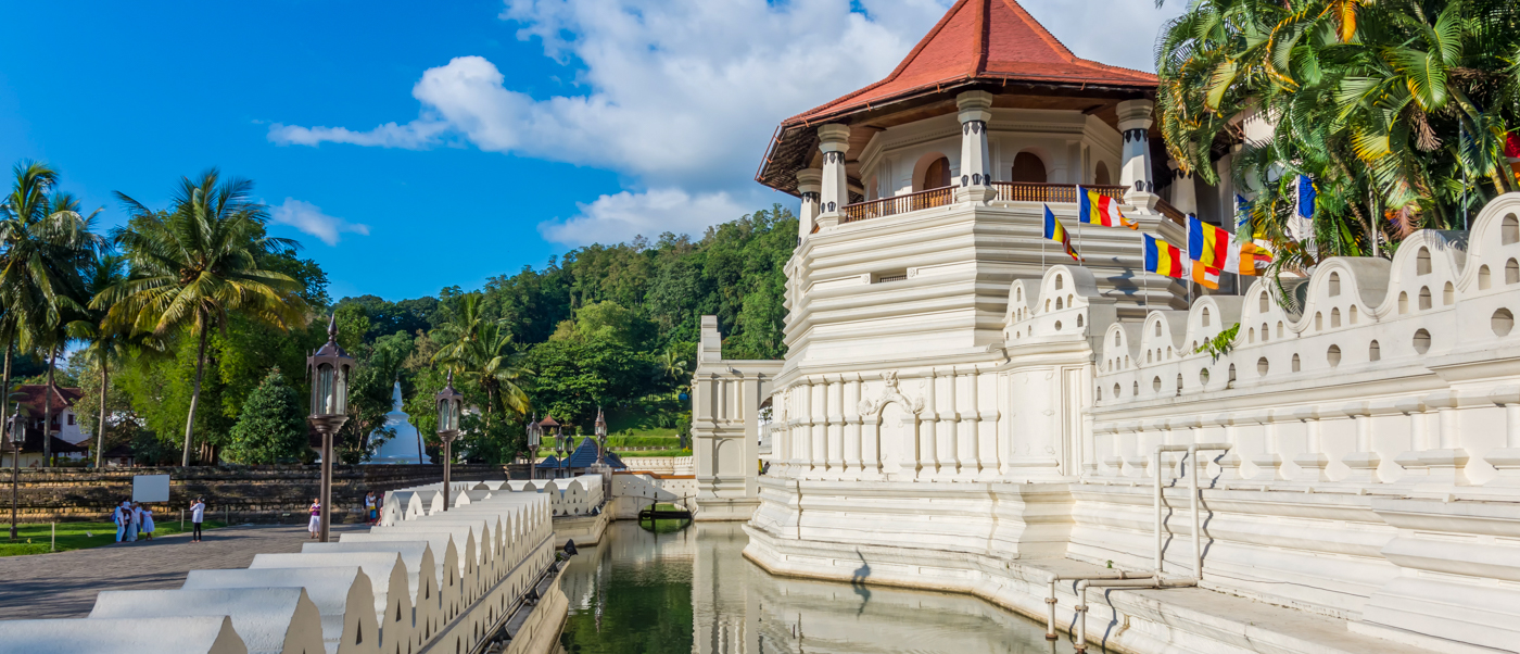 The majestic Temple of the Tooth in Kandy, Sri Lanka, with white walls, a red roof, and a serene moat.