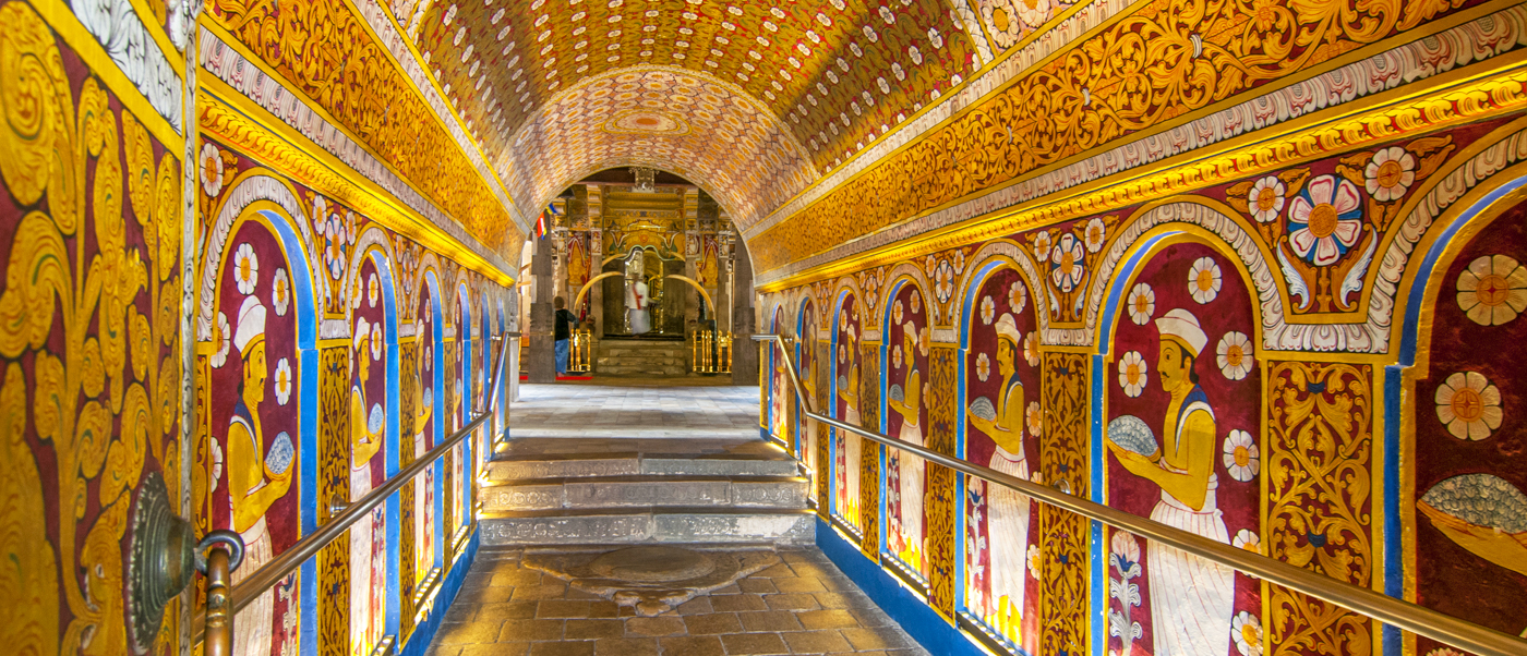 Vibrant ancient murals and golden patterns adorn the arched hallway of the Dambulla Cave Temple.