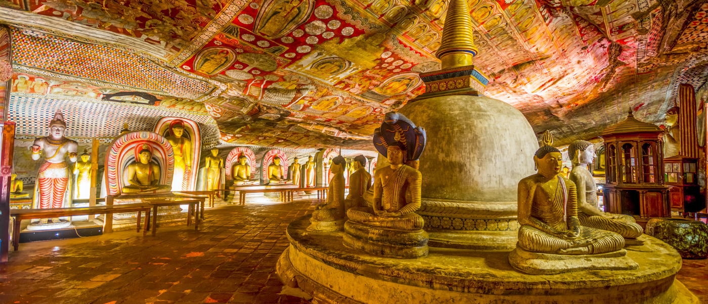 Ancient Dambulla Cave Temple interior with numerous Buddha statues, a stupa, and vibrant ceiling murals.