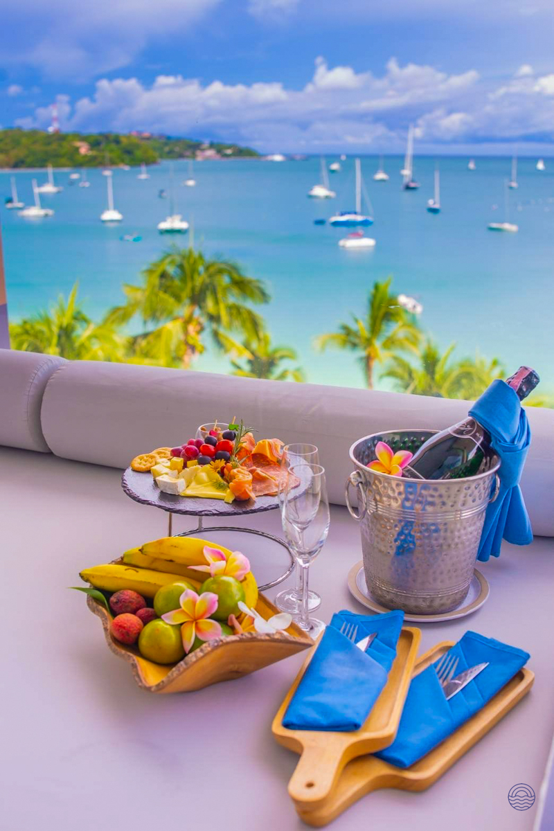 Champagne, fruit, and snacks on a luxurious balcony overlooking a beautiful Phuket bay with sailboats.