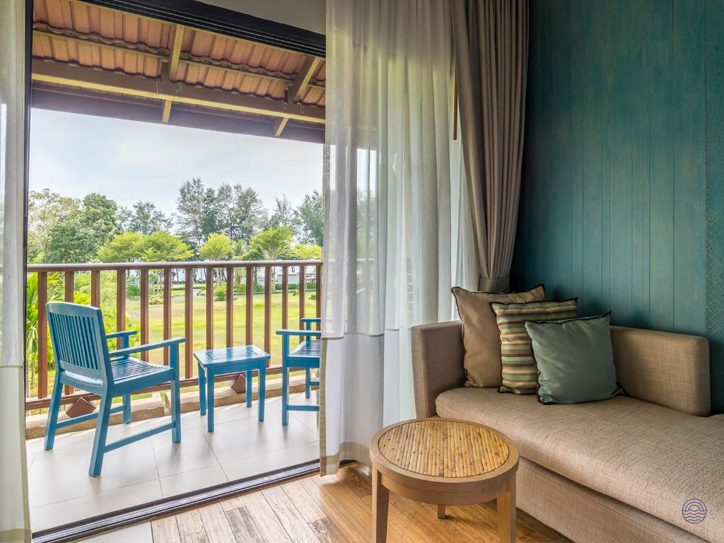 A comfortable hotel room in Krabi with a sofa and a balcony overlooking lush green gardens.