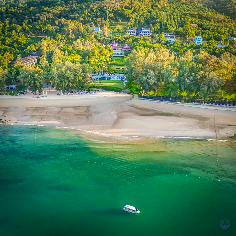 Beautiful tropical beach with green ocean, a boat, and resorts nestled in Krabi's lush coastline.