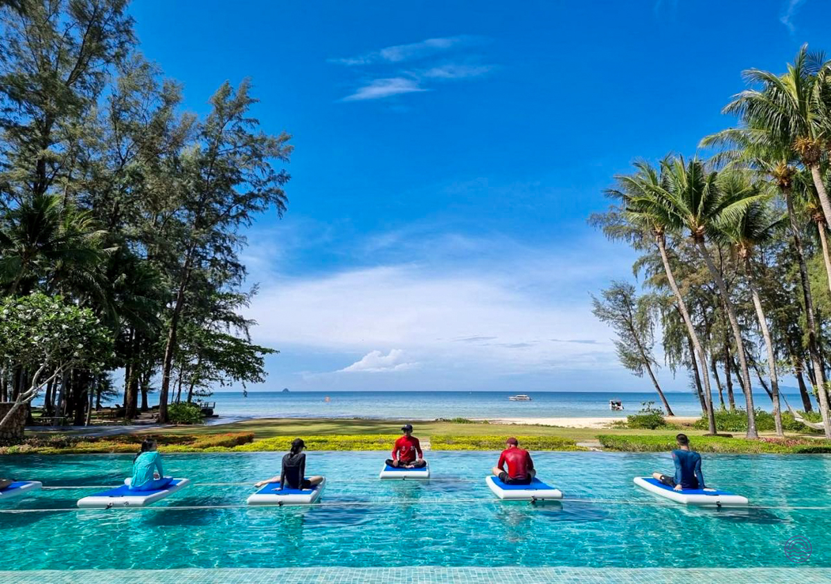 Five people relax on floating mats in an infinity pool overlooking a beautiful Krabi beach.