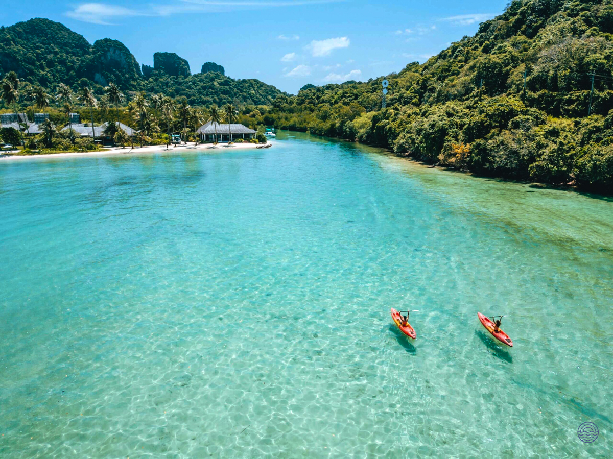 Two kayakers paddle across the crystal-clear turquoise waters of Koh Phi Phi, surrounded by lush green islands.