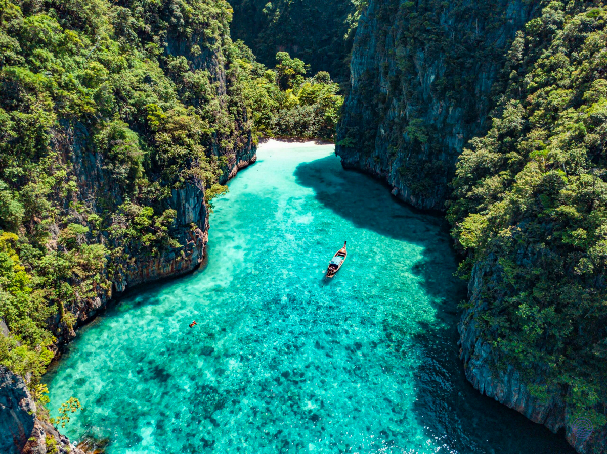 A longtail boat in crystal-clear turquoise waters surrounded by lush green cliffs, Koh Phi Phi.