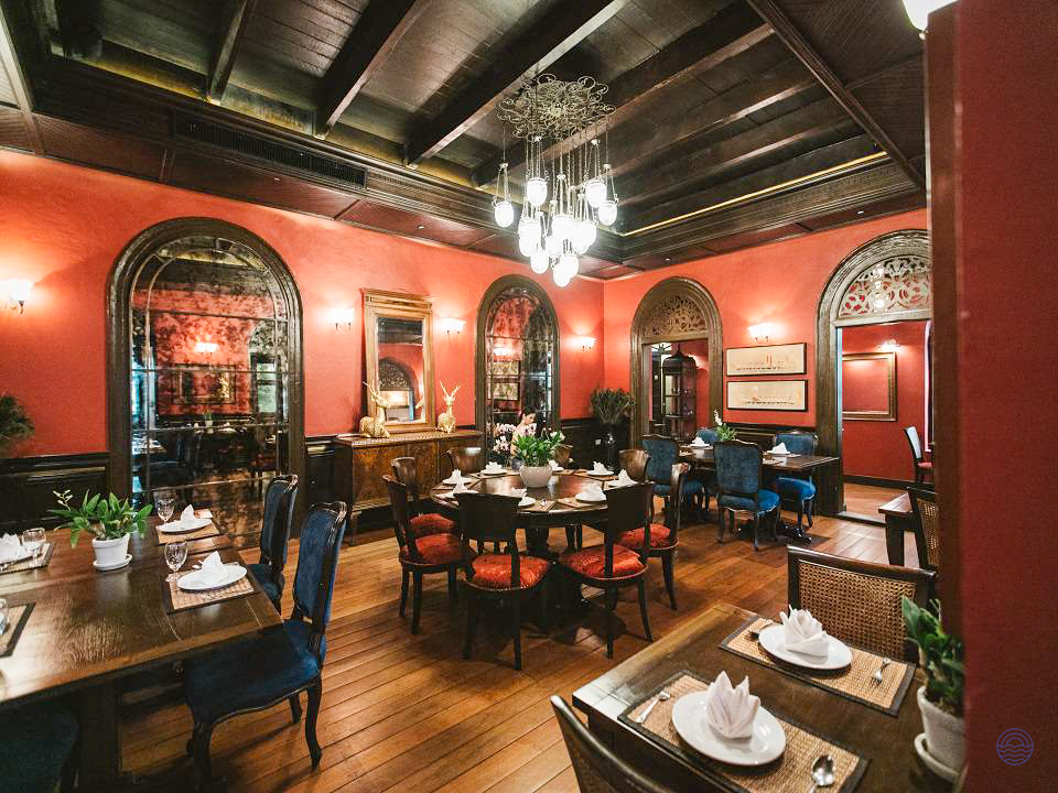 An elegant dining room in Bangkok with rich red walls, dark wood, and luxurious place settings.