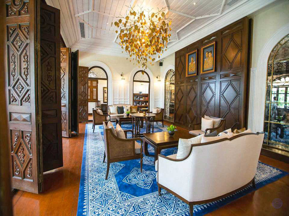 An elegant hotel lounge in Bangkok with a blue patterned rug, comfortable seating, and a unique chandelier.