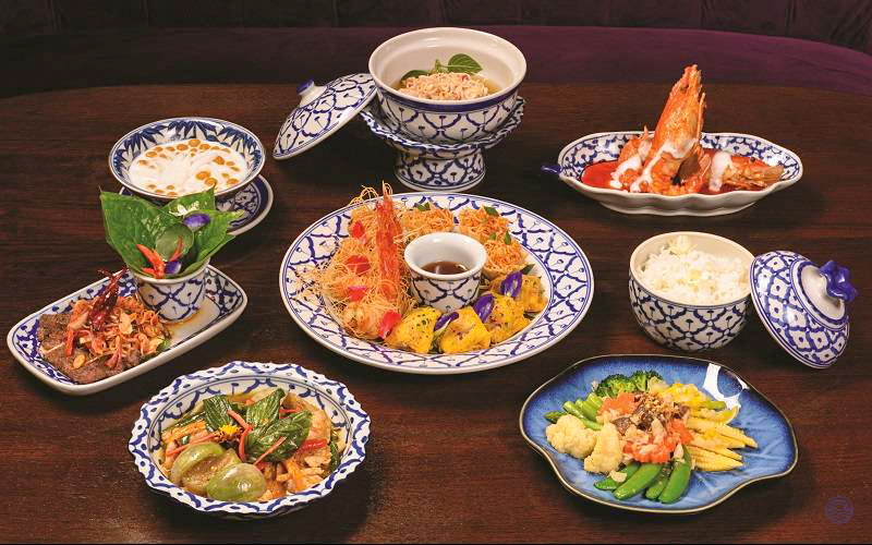 An elegant spread of traditional Thai dishes in ornate blue and white porcelain on a dark wooden table.