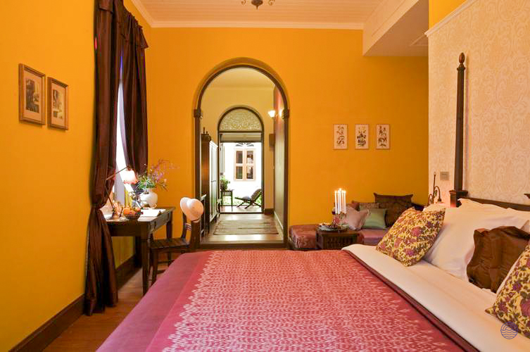 A luxurious hotel room in Bangkok featuring yellow walls, a large bed, and an arched doorway.