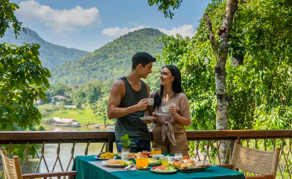 Couple enjoys romantic breakfast on a balcony overlooking a river and mountains in Chiang Mai.