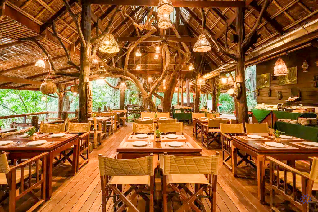 Inviting open-air restaurant with wooden furniture and natural tree structure, ready for guests in Kanchanaburi.
