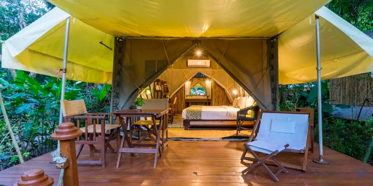 Comfortable glamping tent with a cozy bed and outdoor seating on a wooden deck in Kanchanaburi.