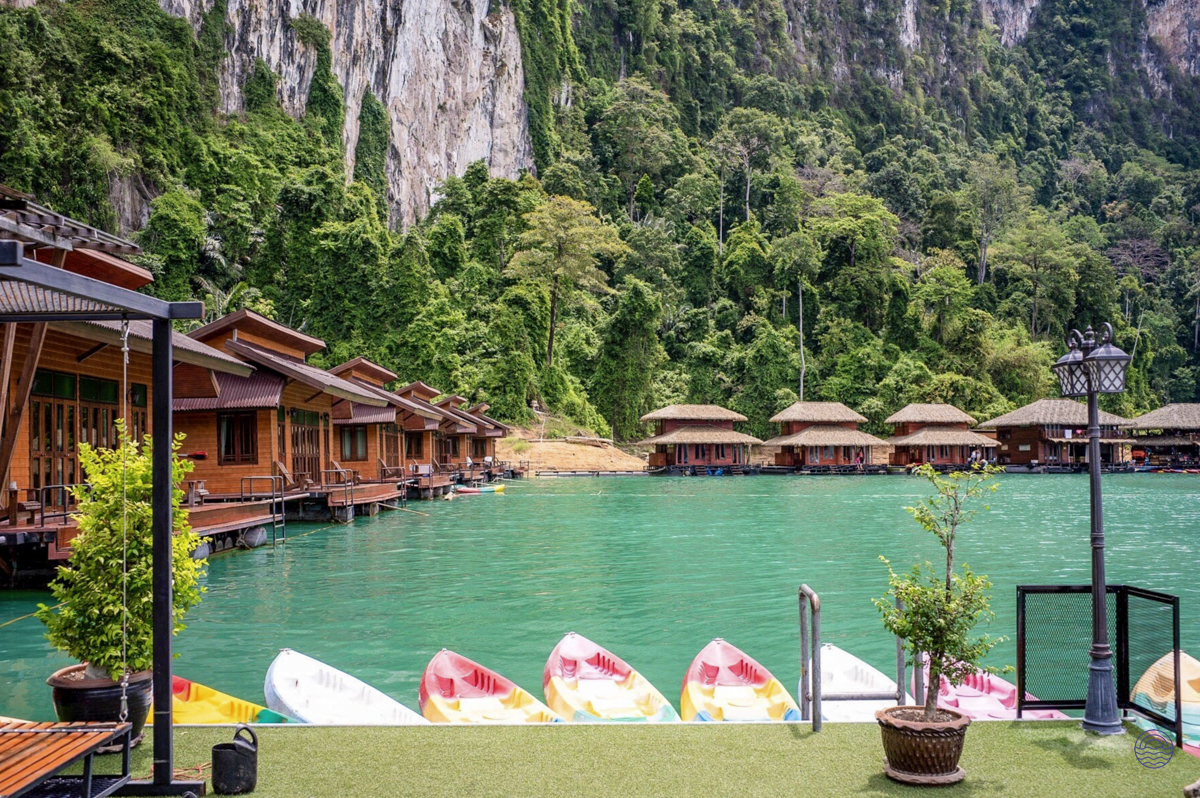 Floating wooden bungalows on a tranquil turquoise lake with kayaks, backed by jungle-covered karsts in Khao Sok.