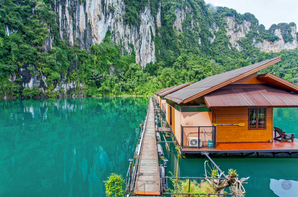 Floating bungalows on a vibrant turquoise lake with dramatic jungle-covered limestone cliffs in Khao Sok.
