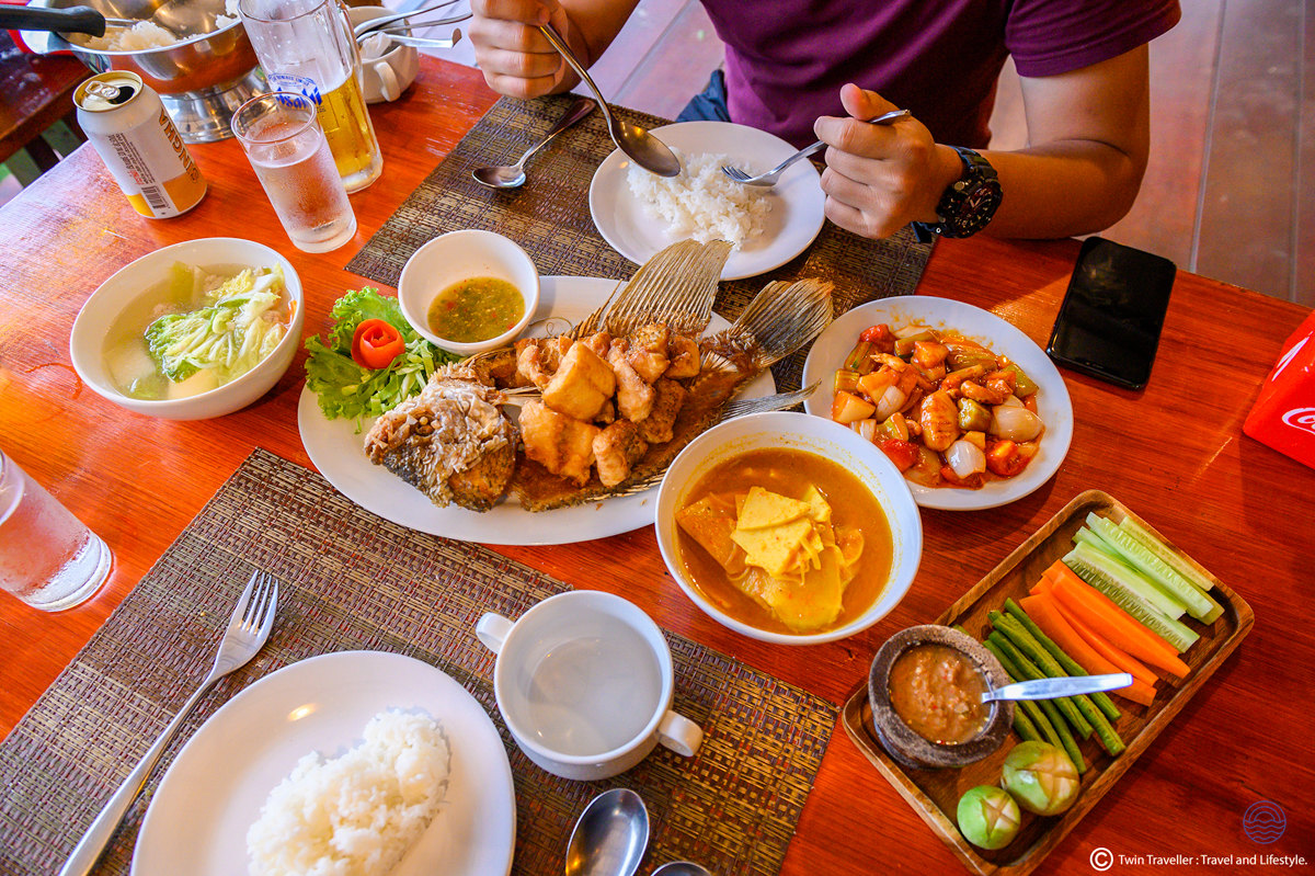 A person enjoys a delicious Thai feast with fried fish, curry, and fresh vegetables on a table.
