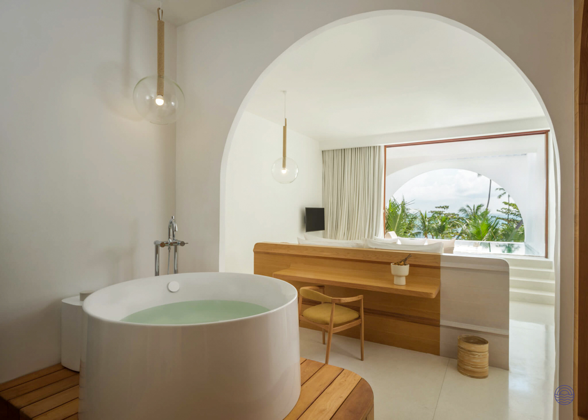 A luxurious hotel suite in Koh Samui with a deep soaking tub and a stunning view of palm trees.