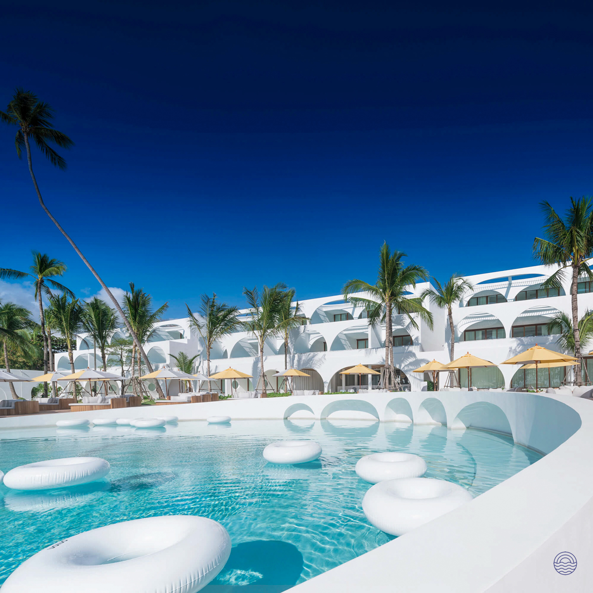 Luxurious white resort with a large swimming pool, white floats, and palm trees on Koh Samui.