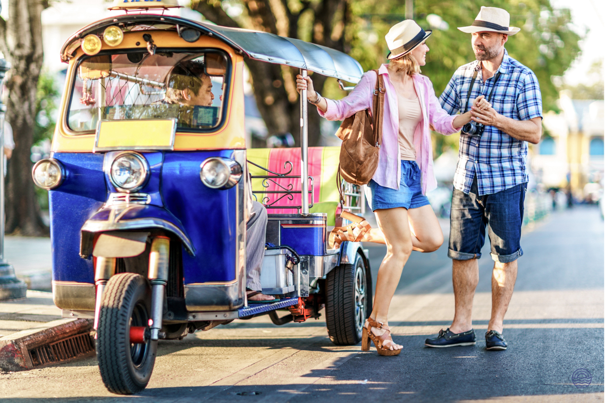 A happy couple explores Bangkok, chatting next to a traditional tuk-tuk on a sunny day.