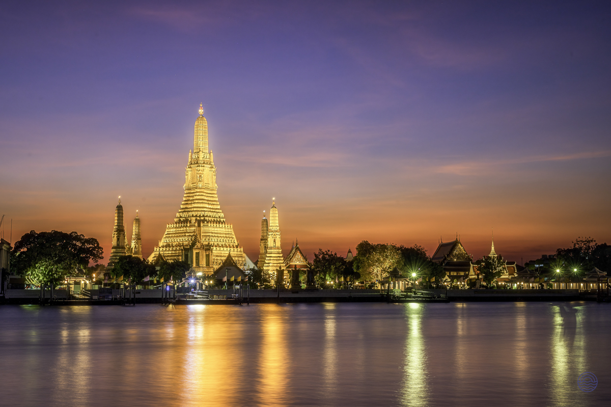 Bangkok's iconic Wat Arun temple glowing golden at dusk, reflecting beautifully on the Chao Phraya River.
