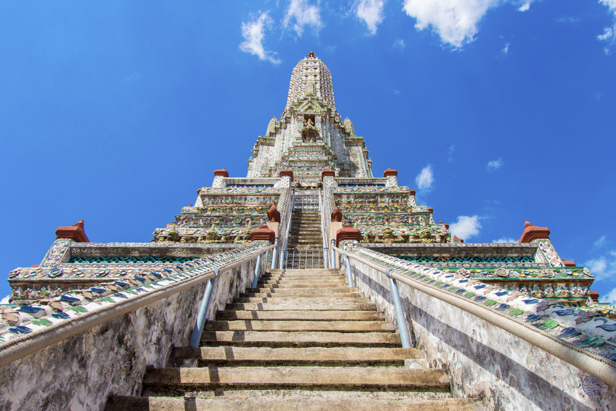 The majestic central prang of Wat Arun temple rises against a clear blue sky in Bangkok.
