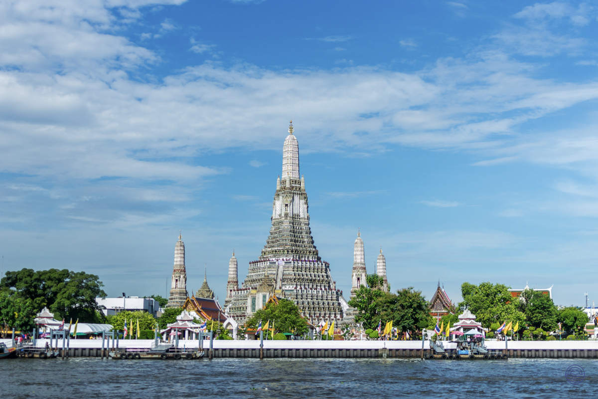 The iconic Wat Arun temple, with its intricate spires, majestically rises above the river in Bangkok.