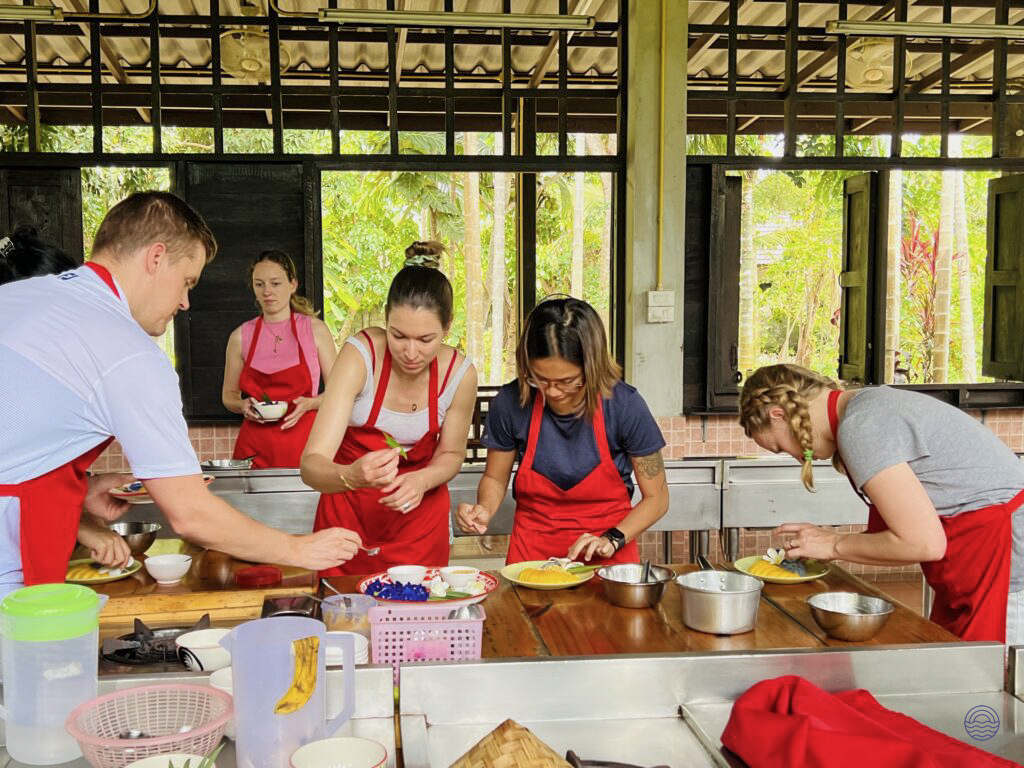 Tourists in red aprons learn to cook Thai dishes at an outdoor cooking school in Chiang Mai.