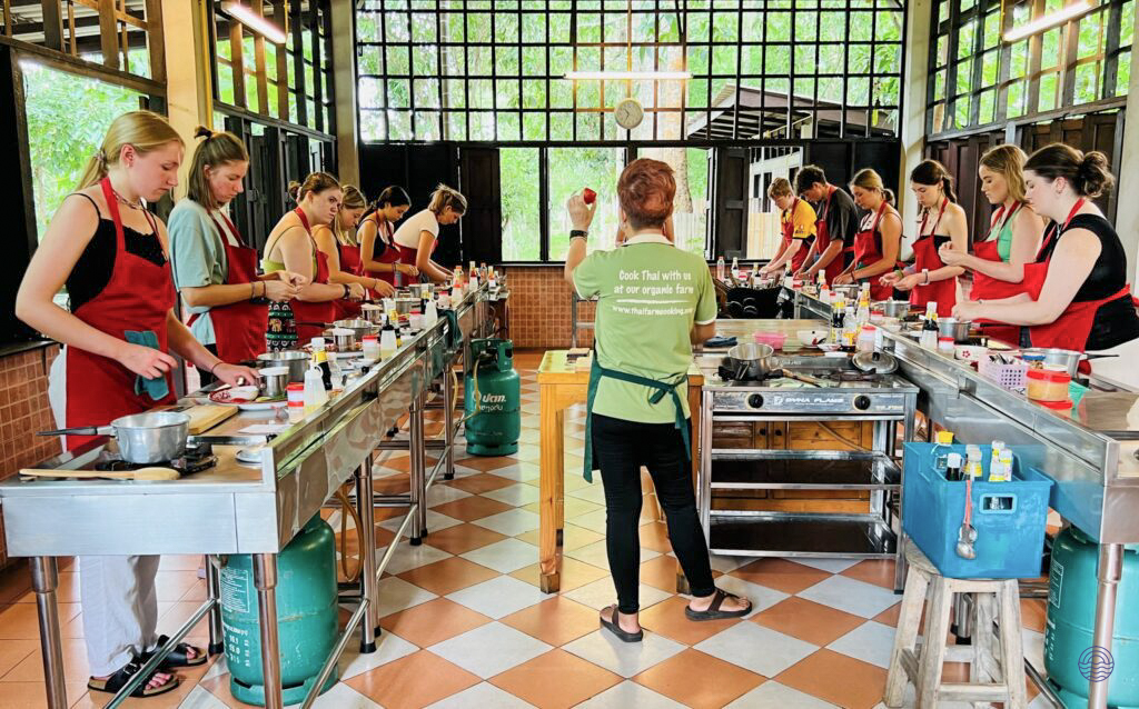 Travelers in red aprons enthusiastically prepare traditional Thai dishes at a cooking class in Chiang Mai.