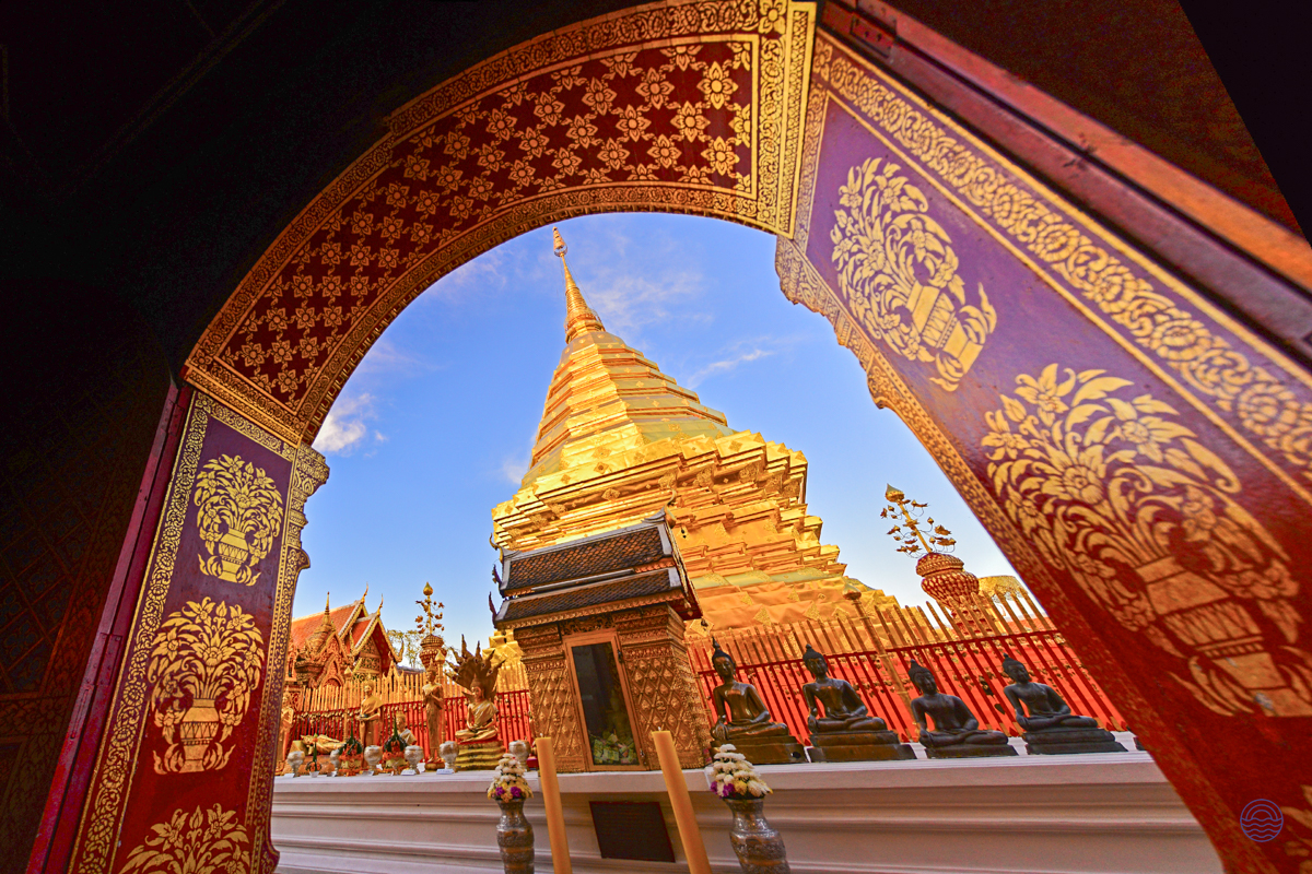Golden chedi of Doi Suthep temple in Chiang Mai, viewed through a richly decorated archway.
