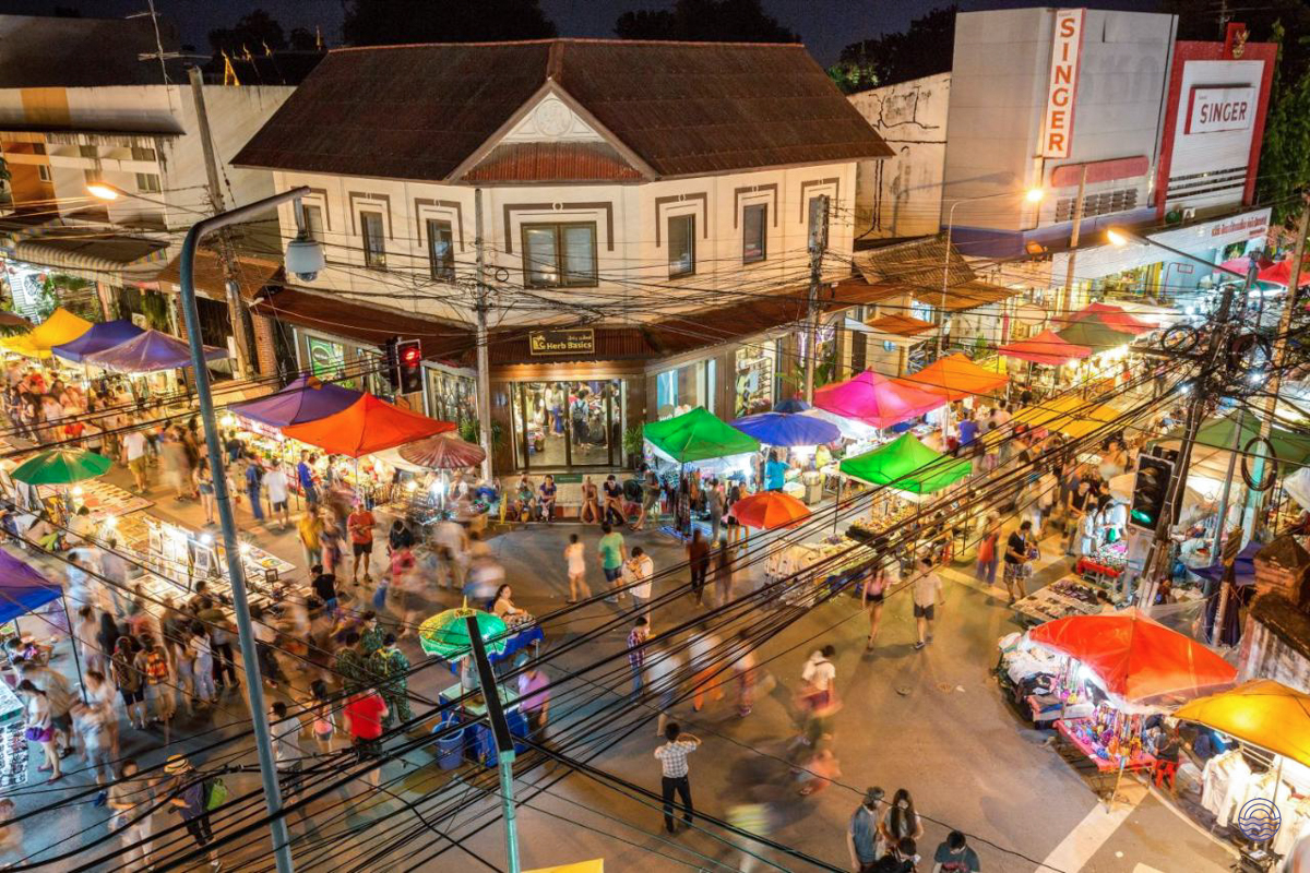 A vibrant night market in Chiang Mai, Thailand, with colorful stalls and many people browsing.