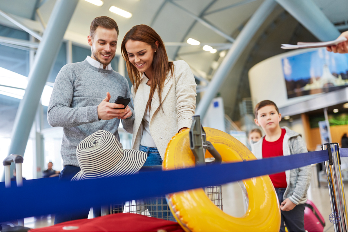 A smiling couple checks their phone at the airport, surrounded by luggage and travel essentials.