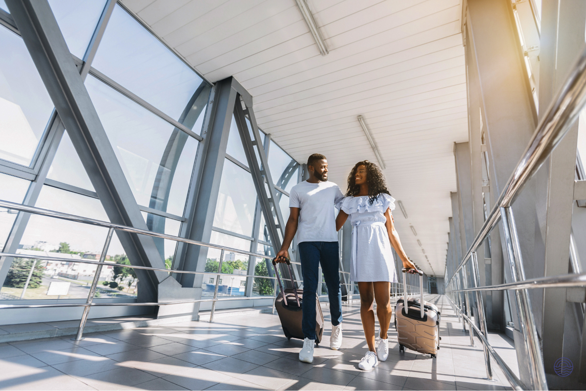 Joyful couple strolls through a sunny airport walkway with suitcases, beginning their tropical getaway.