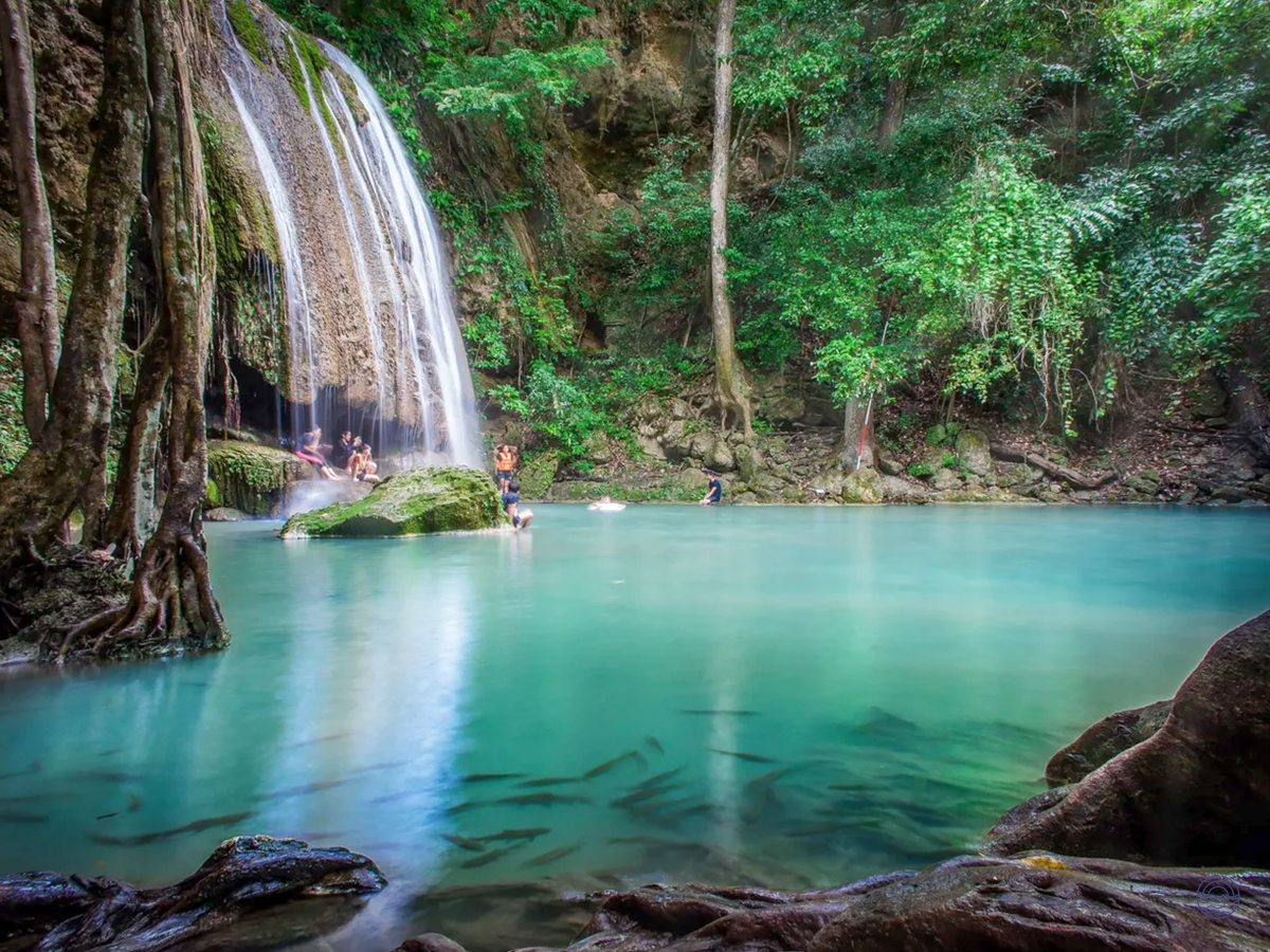 Swimmers enjoy the clear turquoise waters of Erawan Waterfalls in Kanchanaburi, amidst lush jungle.
