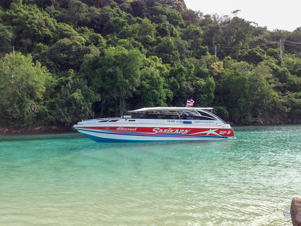A red and white speedboat glides across turquoise waters near lush green islands in Koh Phi Phi.