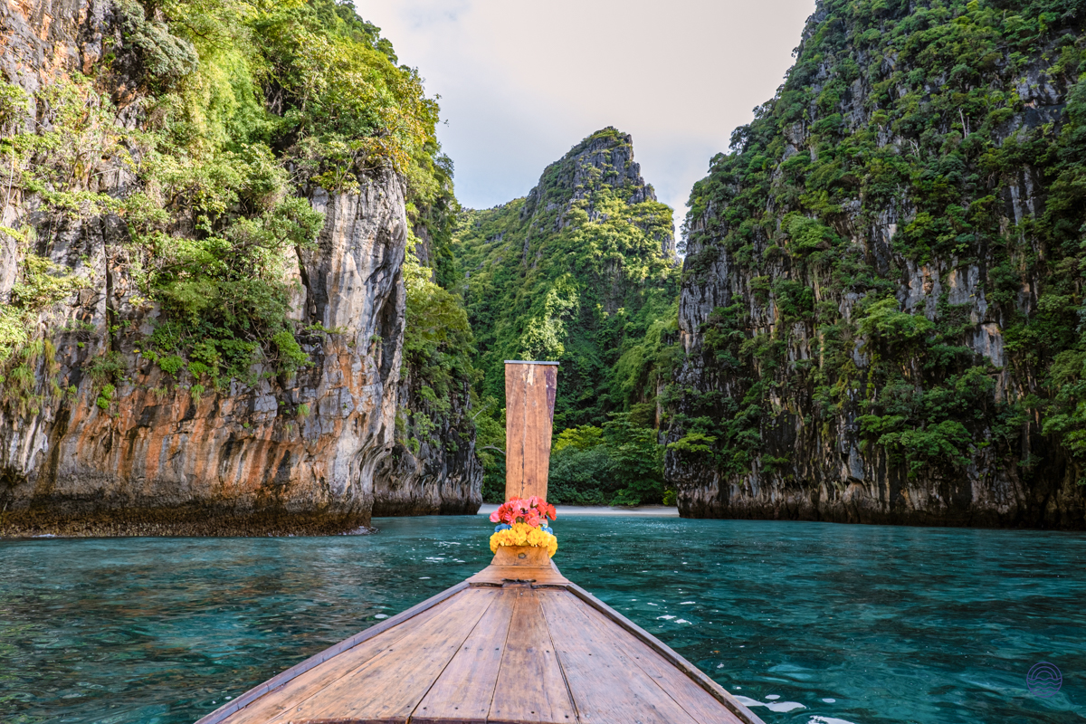 A traditional longtail boat sails through clear turquoise waters, surrounded by towering limestone cliffs in Koh Phi Phi.